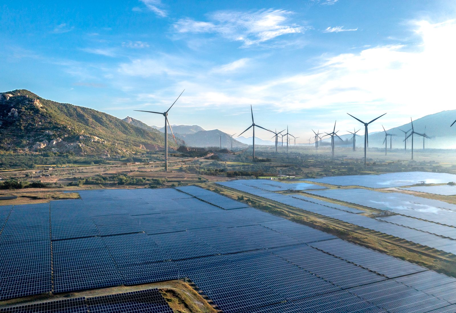 Aerial view of a solar array with wind turbines on the ridge behind it
